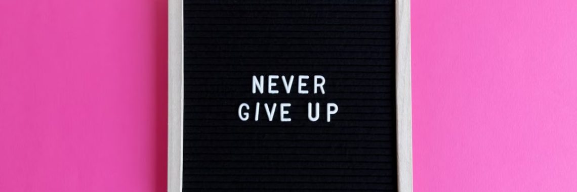 A framed letter board with 'NEVER GIVE UP' on a vibrant pink background.